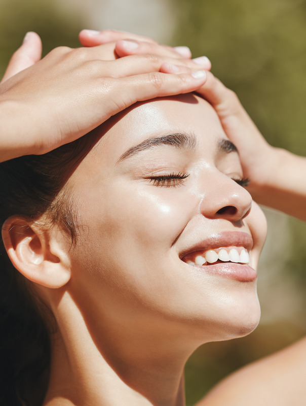 Photo of a smiling woman with great skin outside surrounded by greenery