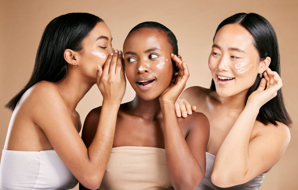 Photo of women wearing skin care products whispering to each other